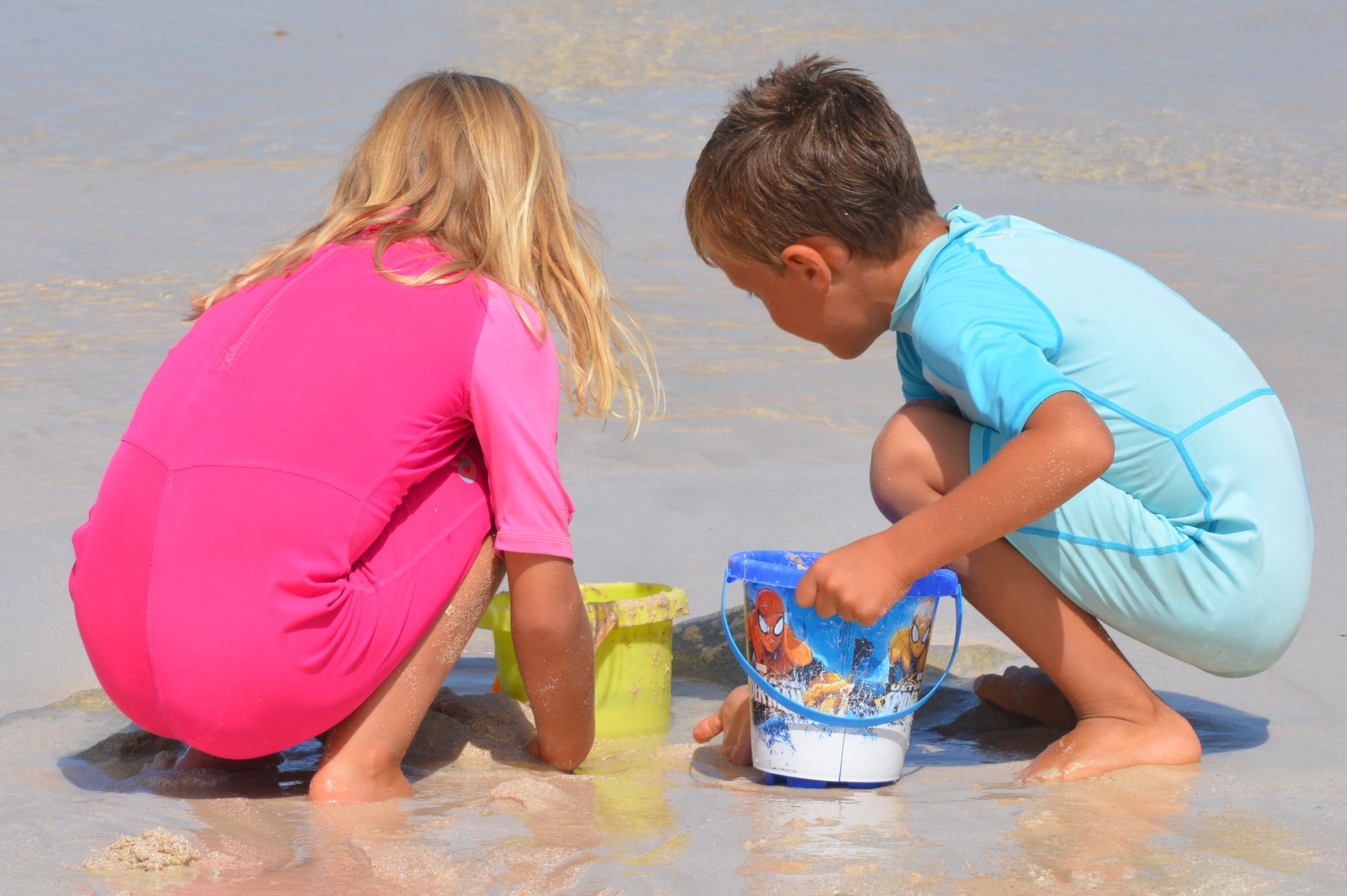 two child playing sand holding plastic buckets during daytime