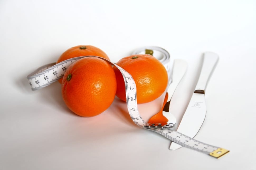 three orange fruits; white plastic tape measure and stainless steel fork and bread knife preview