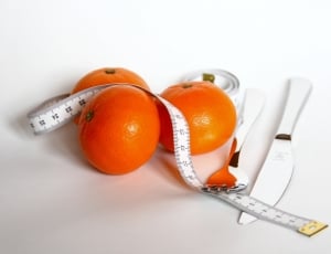 three orange fruits; white plastic tape measure and stainless steel fork and bread knife thumbnail