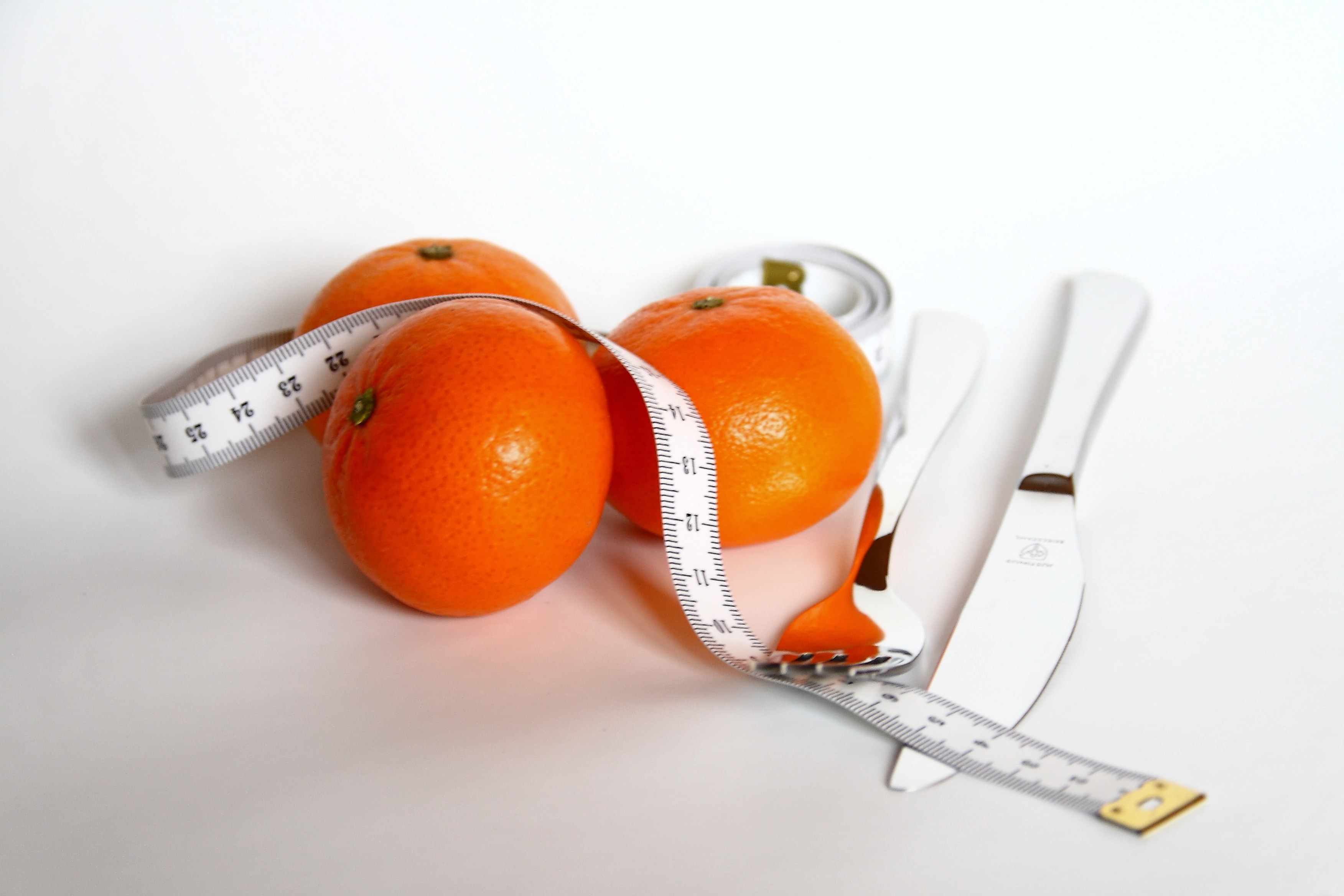 three orange fruits; white plastic tape measure and stainless steel fork and bread knife