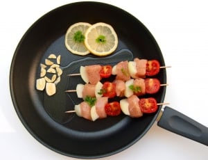 black cooking pot with meat and tomato skewers with lemon slices thumbnail
