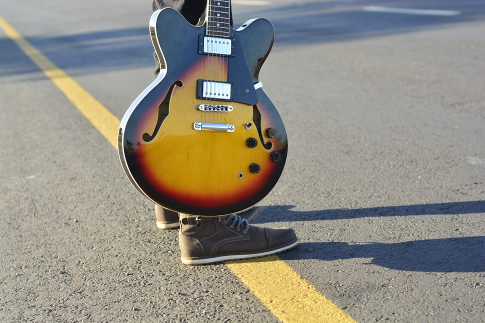 person holding sunburst electric guitar standing in the middle of road during daytime preview