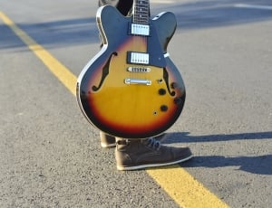 person holding sunburst electric guitar standing in the middle of road during daytime thumbnail
