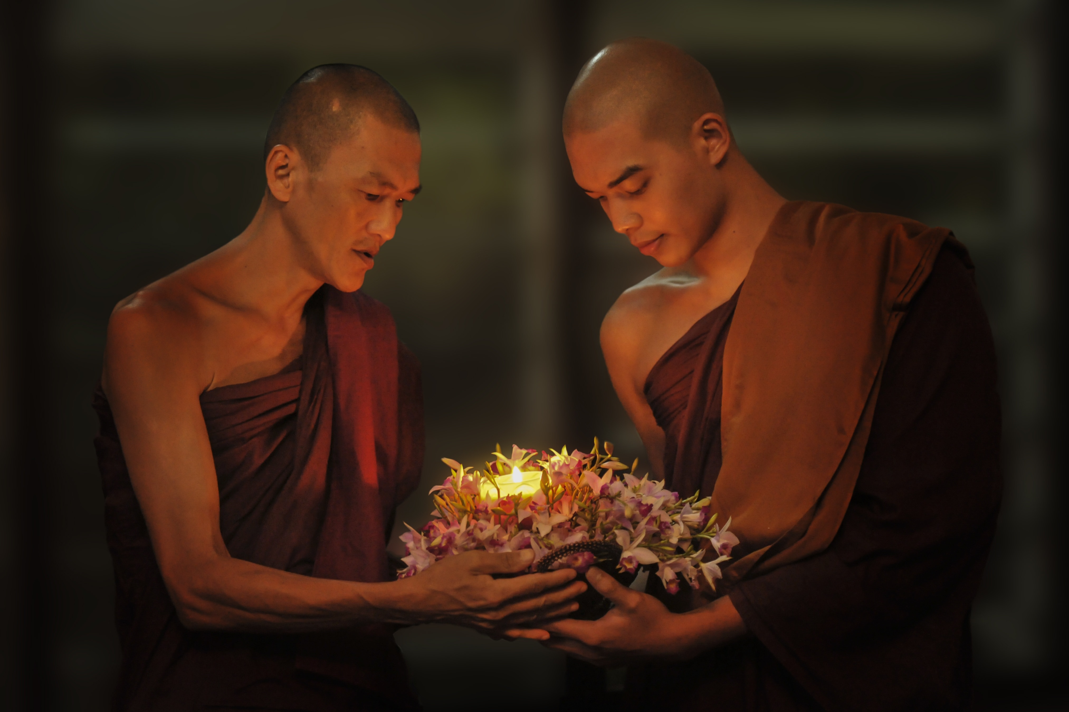 2 men in brown robe holding brown floral candle stand