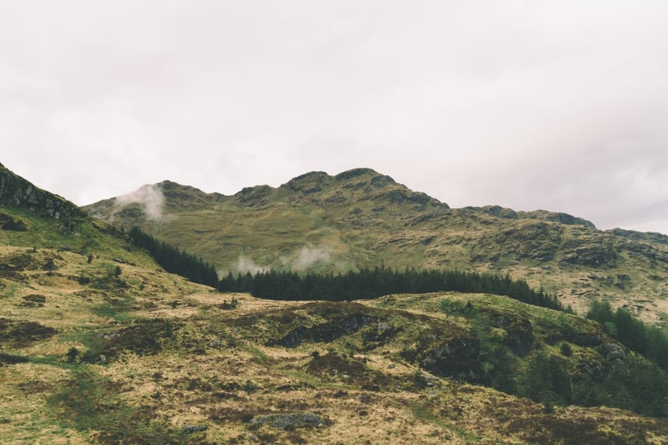 green trees on mountains under gray cloudy sky during daytime preview