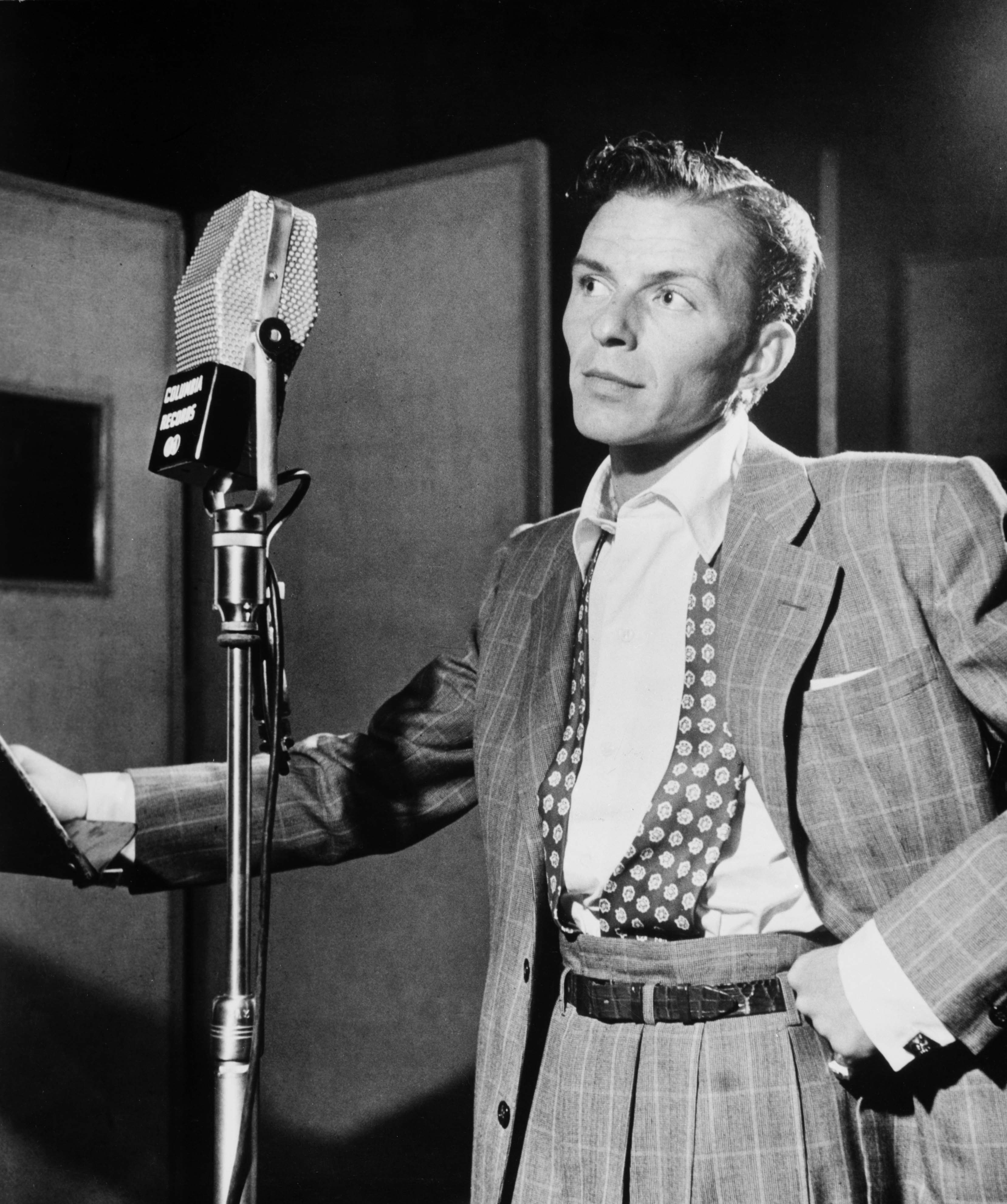 gray scale photo of man in formal suit standing near microphone