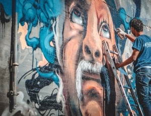 man's face mural painting; men's blue t-shirt and blue denim jeans thumbnail