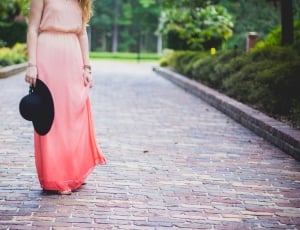 woman wearing white and peach ombre sleeveless gathered waist dress holding hat and standing on paved pathway during daytime thumbnail