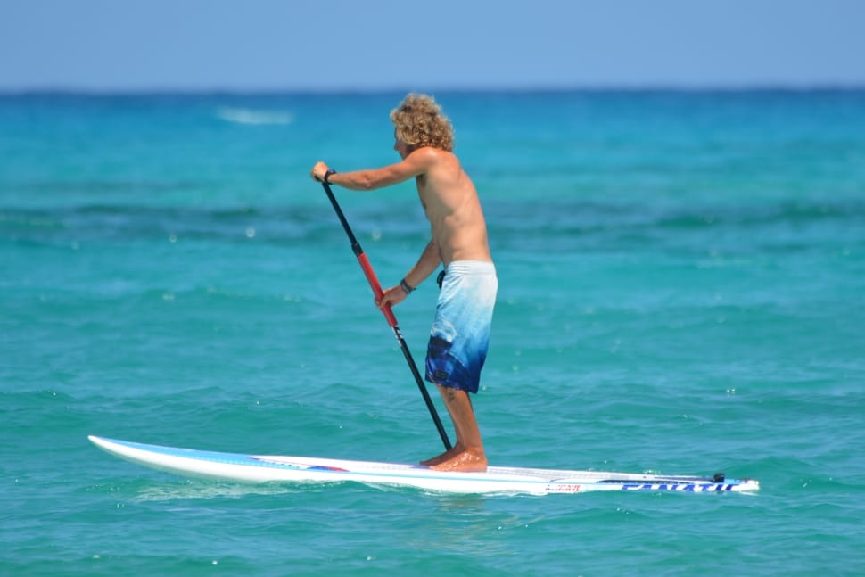 man in white and blue board-shorts standing on white surfboard during daytime preview
