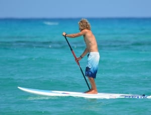 man in white and blue board-shorts standing on white surfboard during daytime thumbnail