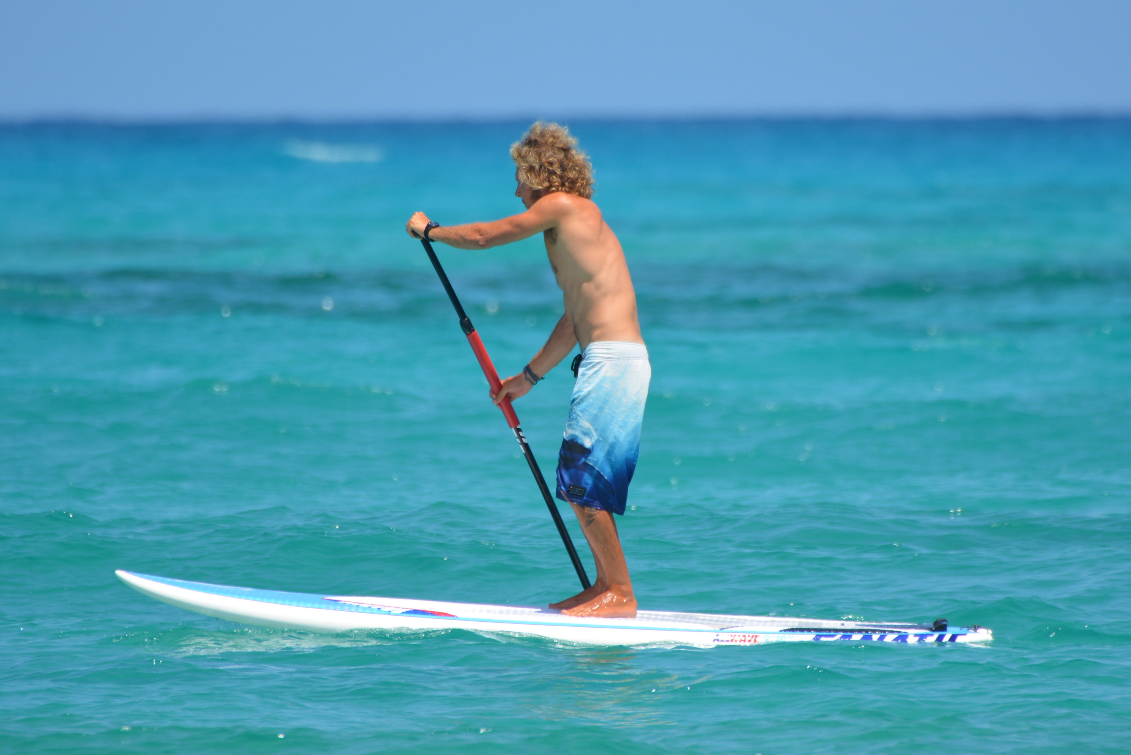 man in white and blue board-shorts standing on white surfboard during daytime