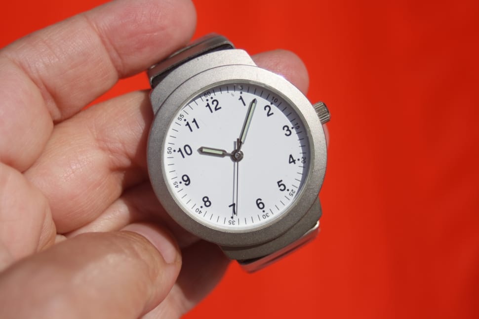 person holding round silver framed analog watch at 10:07 preview