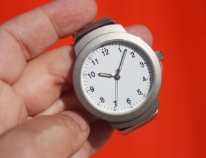 person holding round silver framed analog watch at 10:07 thumbnail