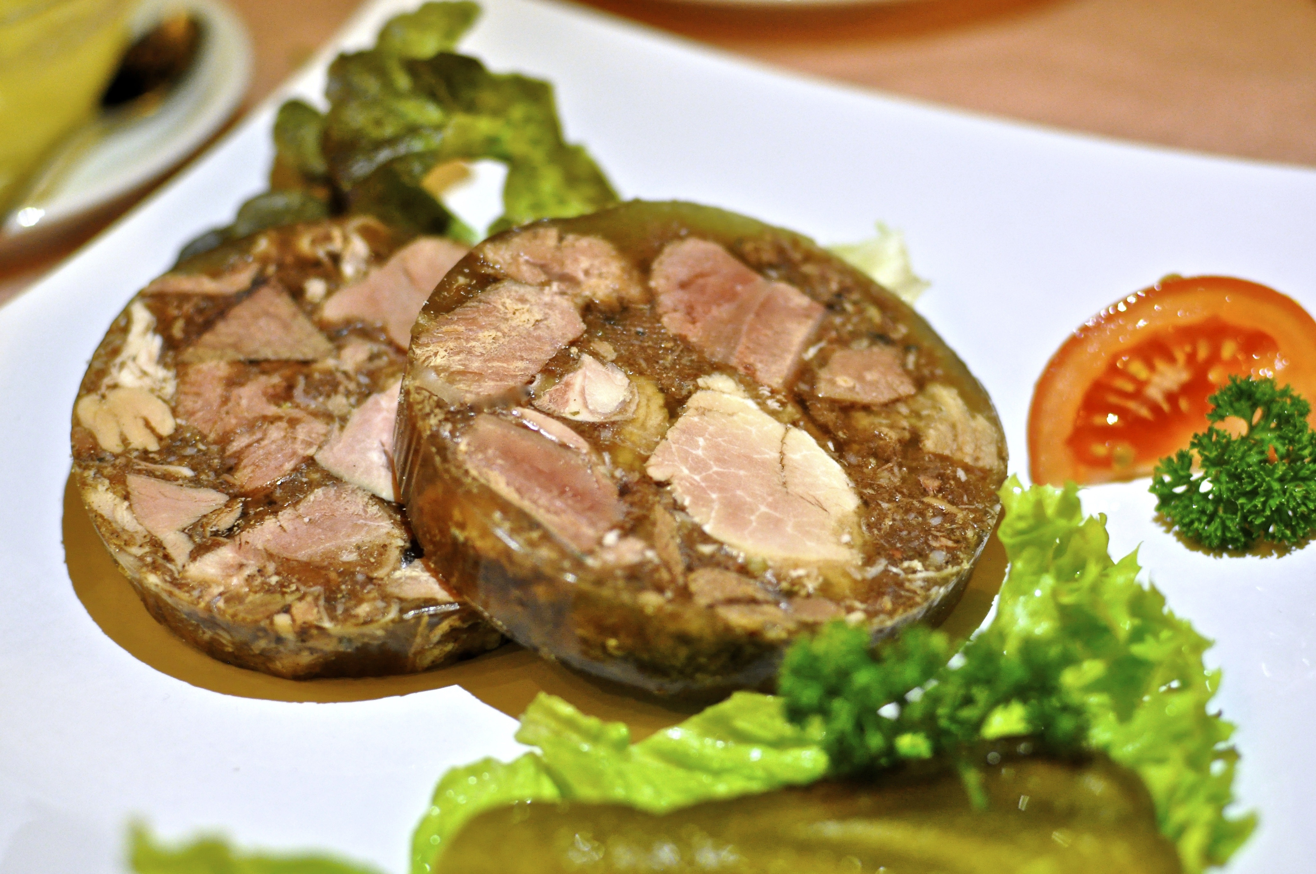 two meat dishes with green leafy vegetable and sliced tomato on white ceramic plate