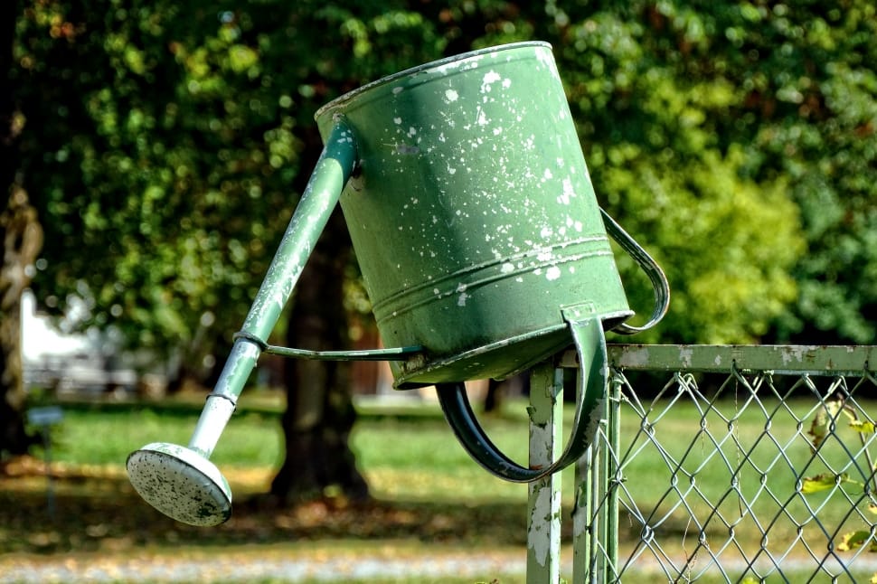 green watering can on green metal chain link fence preview