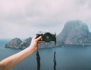 person holding digital camera under cloudy sky during daytime thumbnail