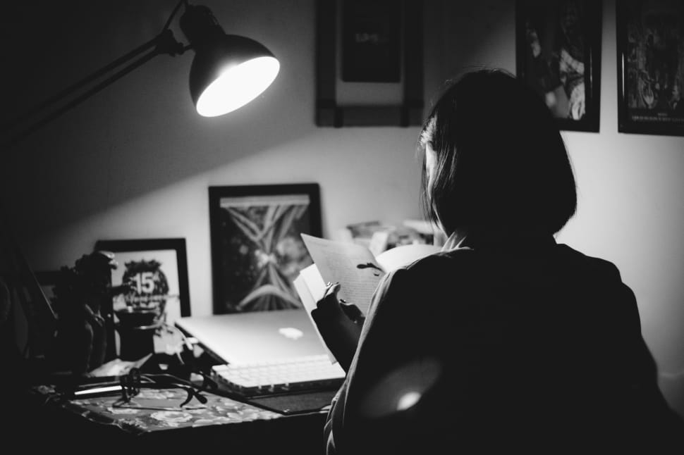 grey scale photography of woman reading book infront of desk preview