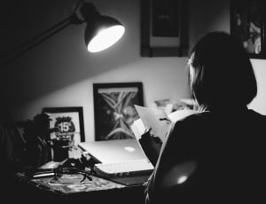 grey scale photography of woman reading book infront of desk thumbnail