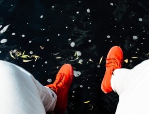 person wearing orange lace-up shoes sitting near body of water thumbnail