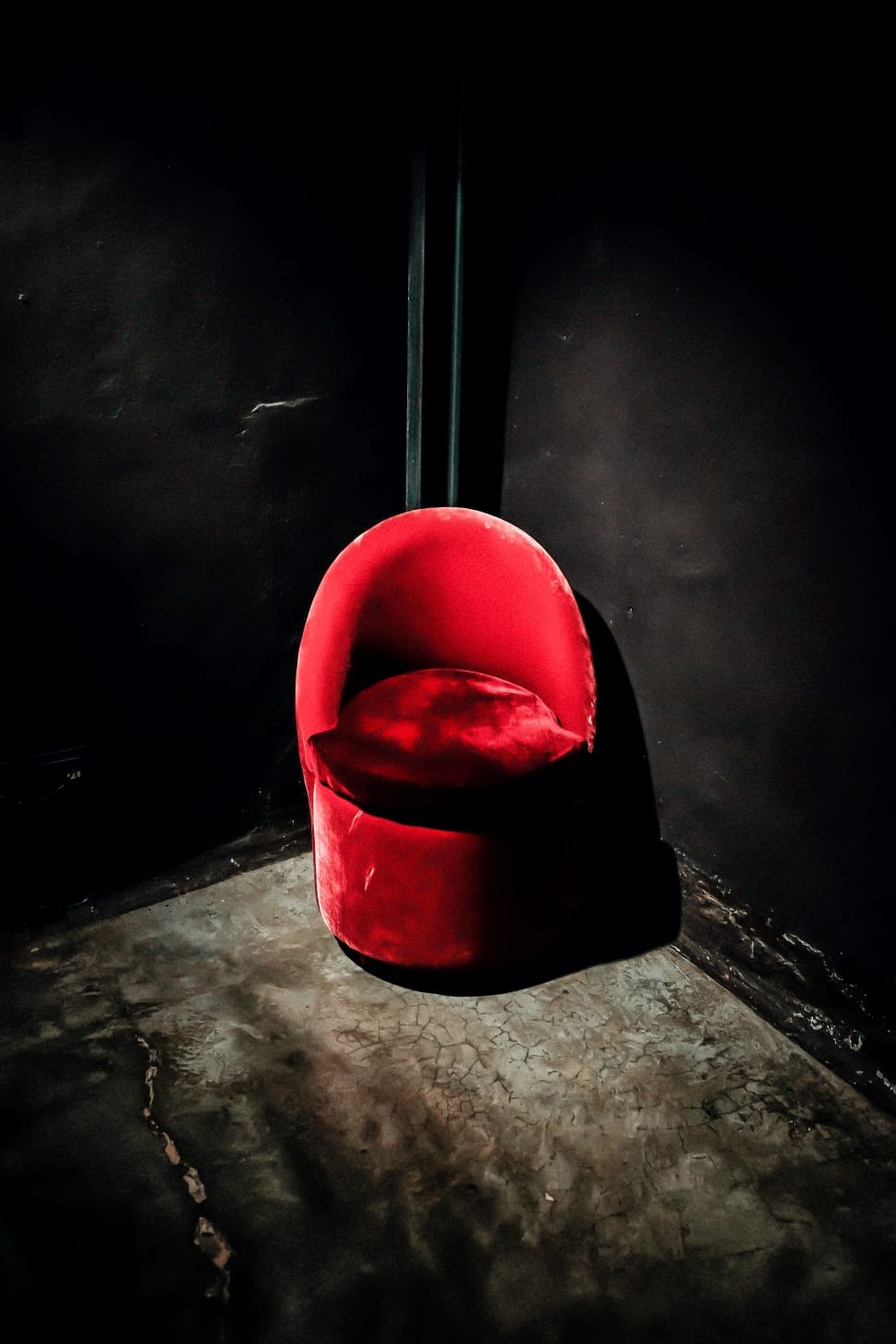 red suede chair in the corner of black wall paint room preview