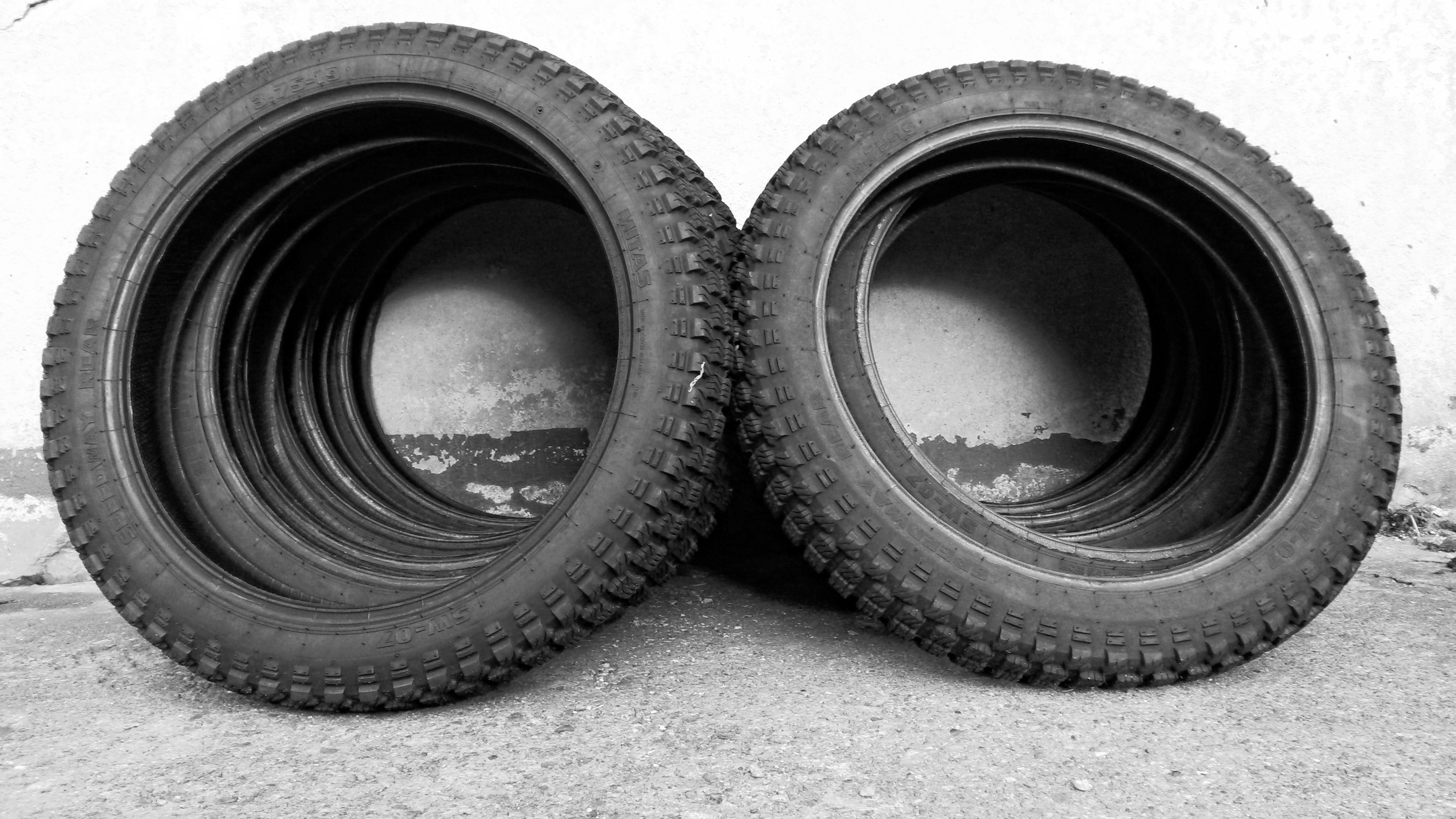 grayscale photo of motorcycles wheels leaning on wall