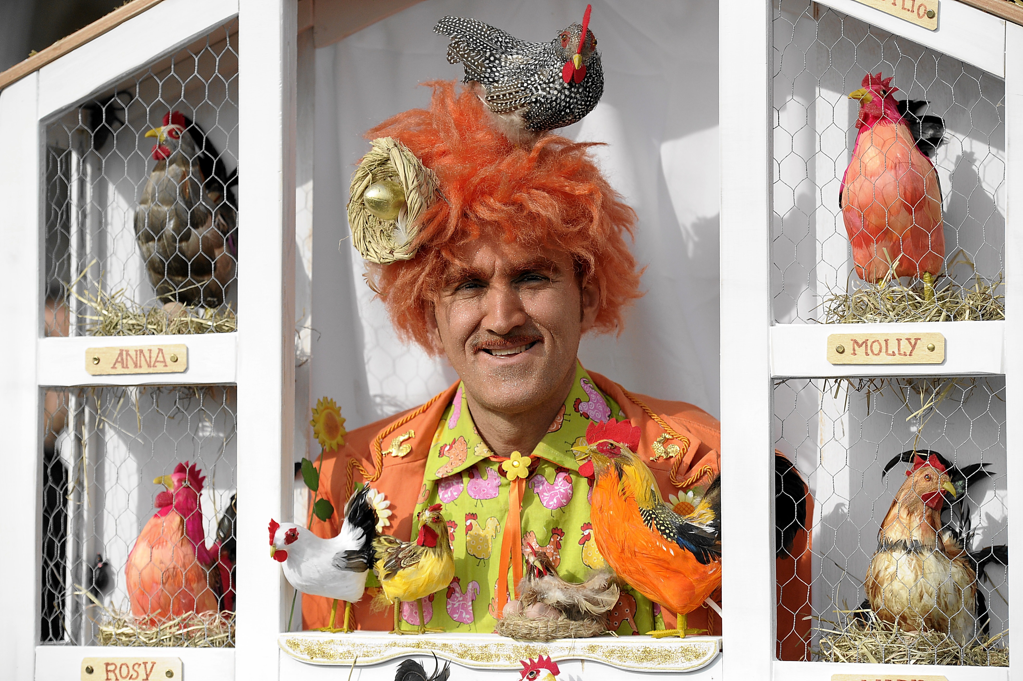 man in orange formal suit jacket surrounded of roosters and chicks toys