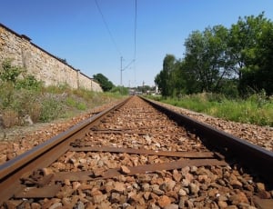 railroad beside trees near brick wall during daytime thumbnail
