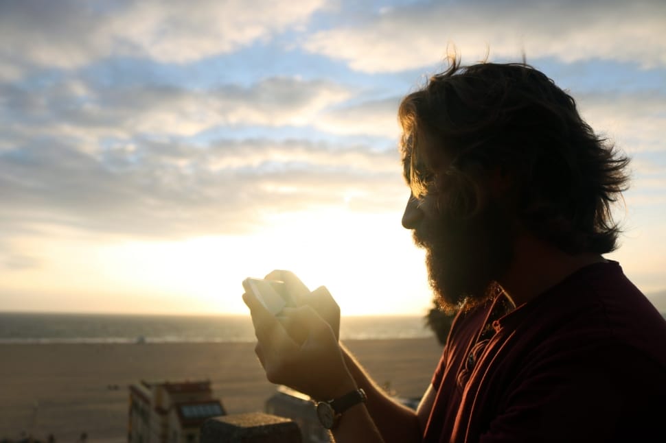 man wearing red shirt holding device during sun set preview