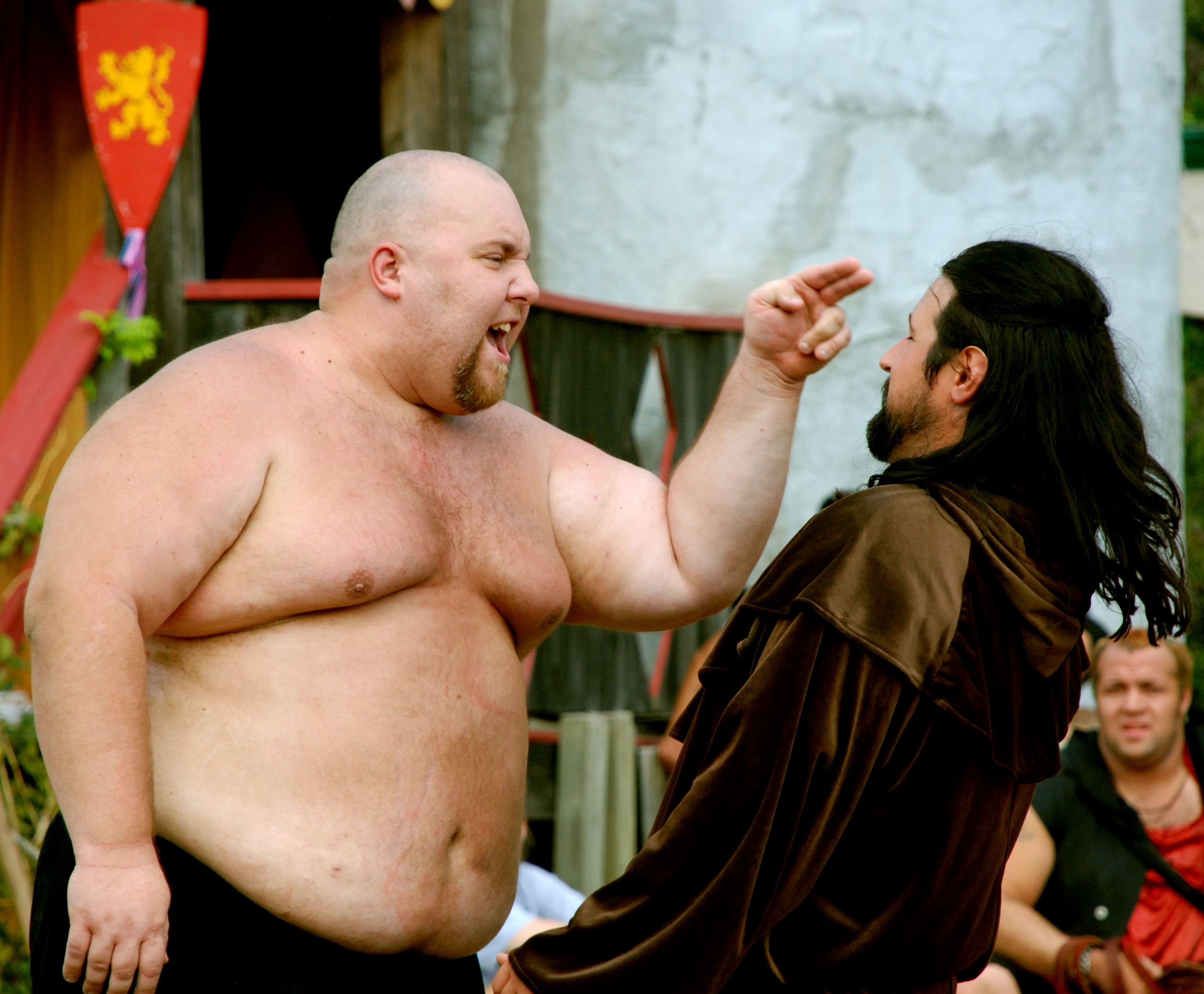 fat and bald shirtless man pointing his finger at a long-haired bearded man