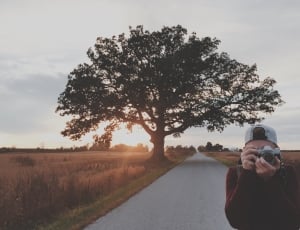 person in brown sweater holding grey camera thumbnail