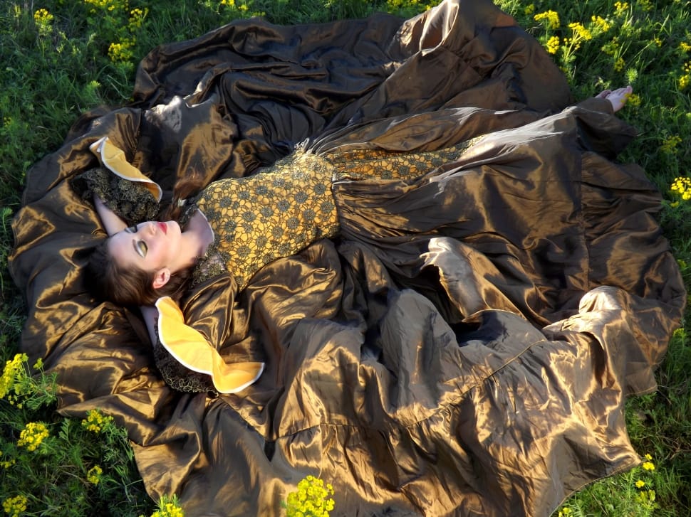 woman in yelow and black ruffled dress lying down on yellow flowers during daytime preview