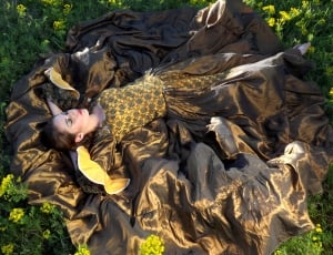 woman in yelow and black ruffled dress lying down on yellow flowers during daytime thumbnail