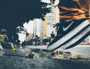 close up photography of person in black nike low top sneakers, brown jeans jumped on wet asphalt road way thumbnail