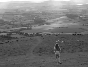 grayscale photo of girl walking on hills thumbnail