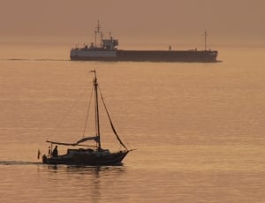 sailboat and ship in the sea under grey sky thumbnail