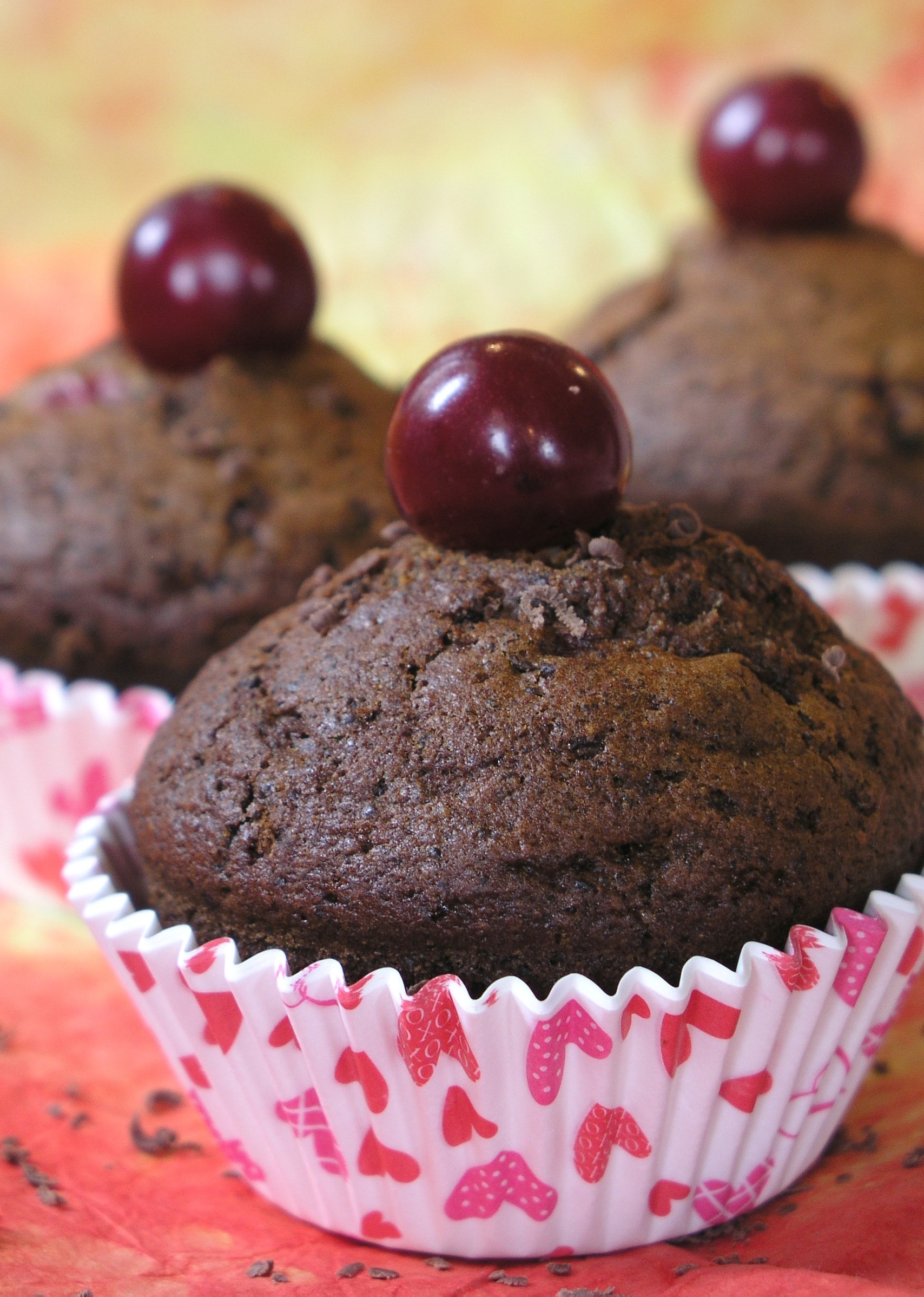 three chocolate muffins with red berry on top