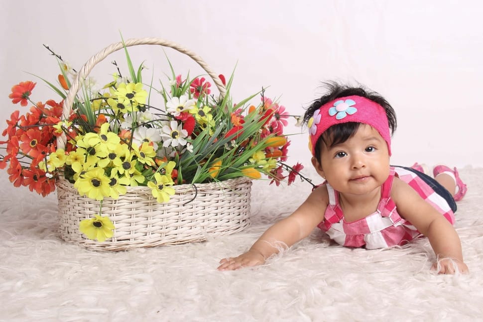 baby's pink and white dress and brown wicker basket with red and yellow petal flower preview