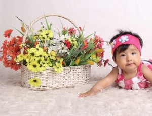 baby's pink and white dress and brown wicker basket with red and yellow petal flower thumbnail