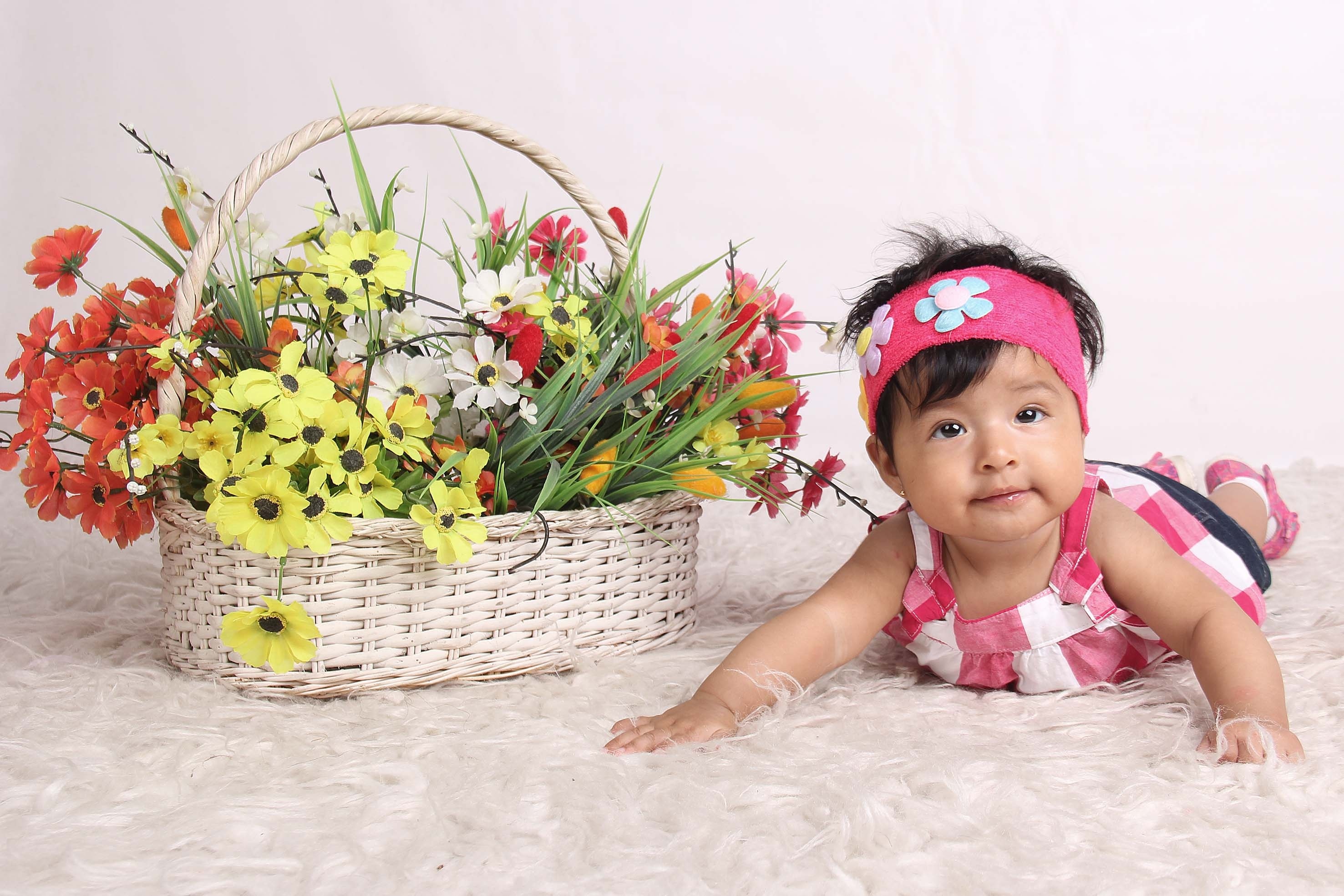 baby's pink and white dress and brown wicker basket with red and yellow petal flower