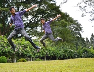 two men jumping on green open field during daytime thumbnail