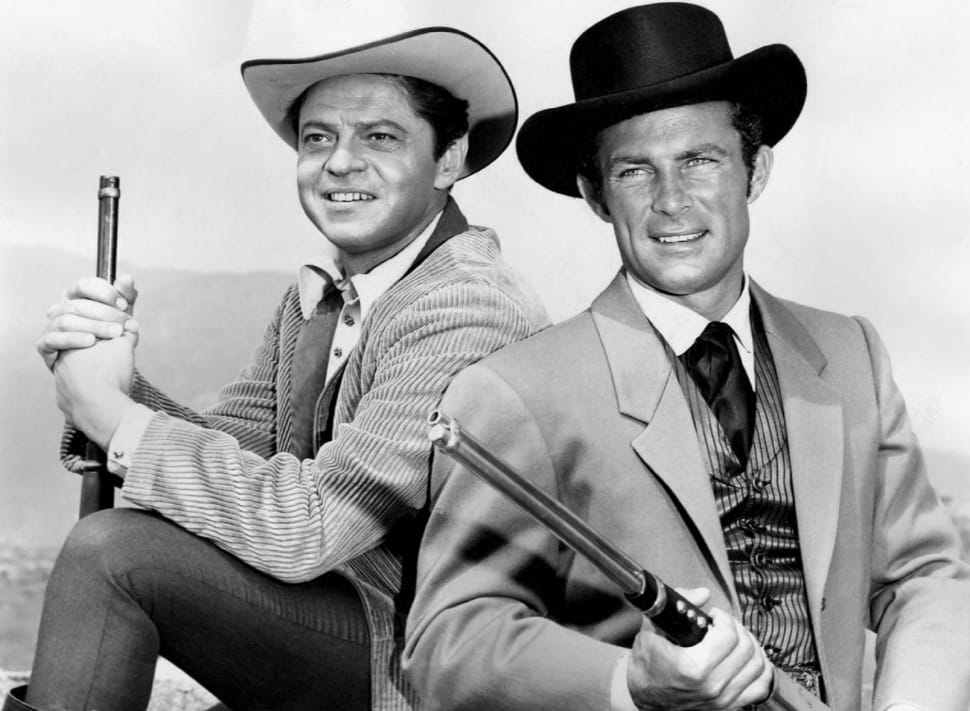 grayscale photo of two men with hats holding guns and smiling preview