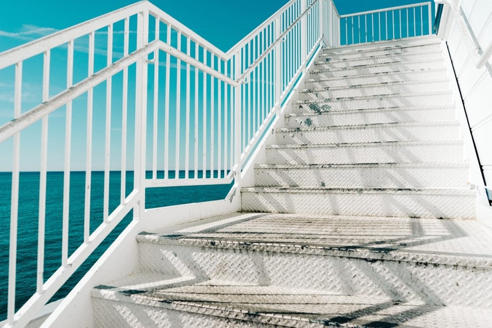 shallow focus photography of white steel staircase near blue ocean water during daytime preview