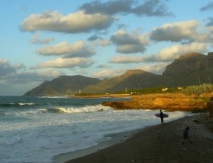 photo of ocean with man with surfboard on seashore during day time thumbnail