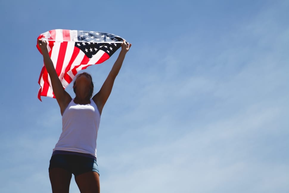 woman in white tank top standing holding u.s.a flag preview