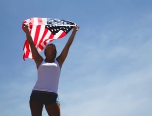 woman in white tank top standing holding u.s.a flag thumbnail