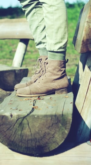 person wearing brown leather lace up boots standing on log thumbnail