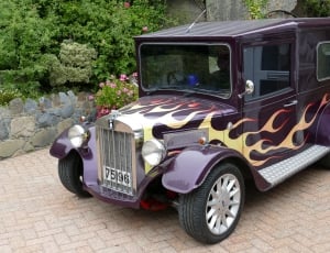 purple classic costume flame painted car parked on brown bricked surface at daytime thumbnail