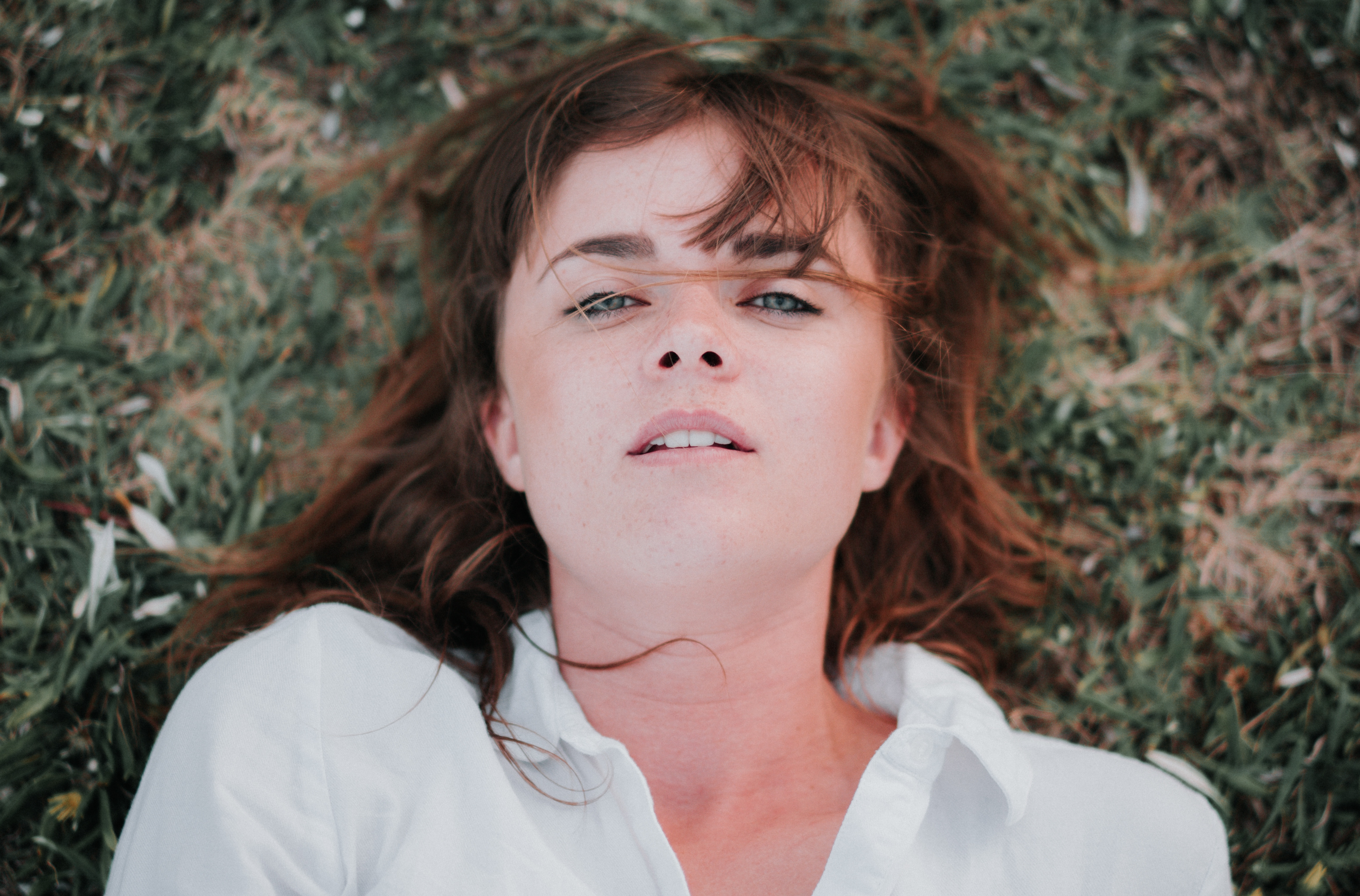 woman wearing white button up shirt lying on grass