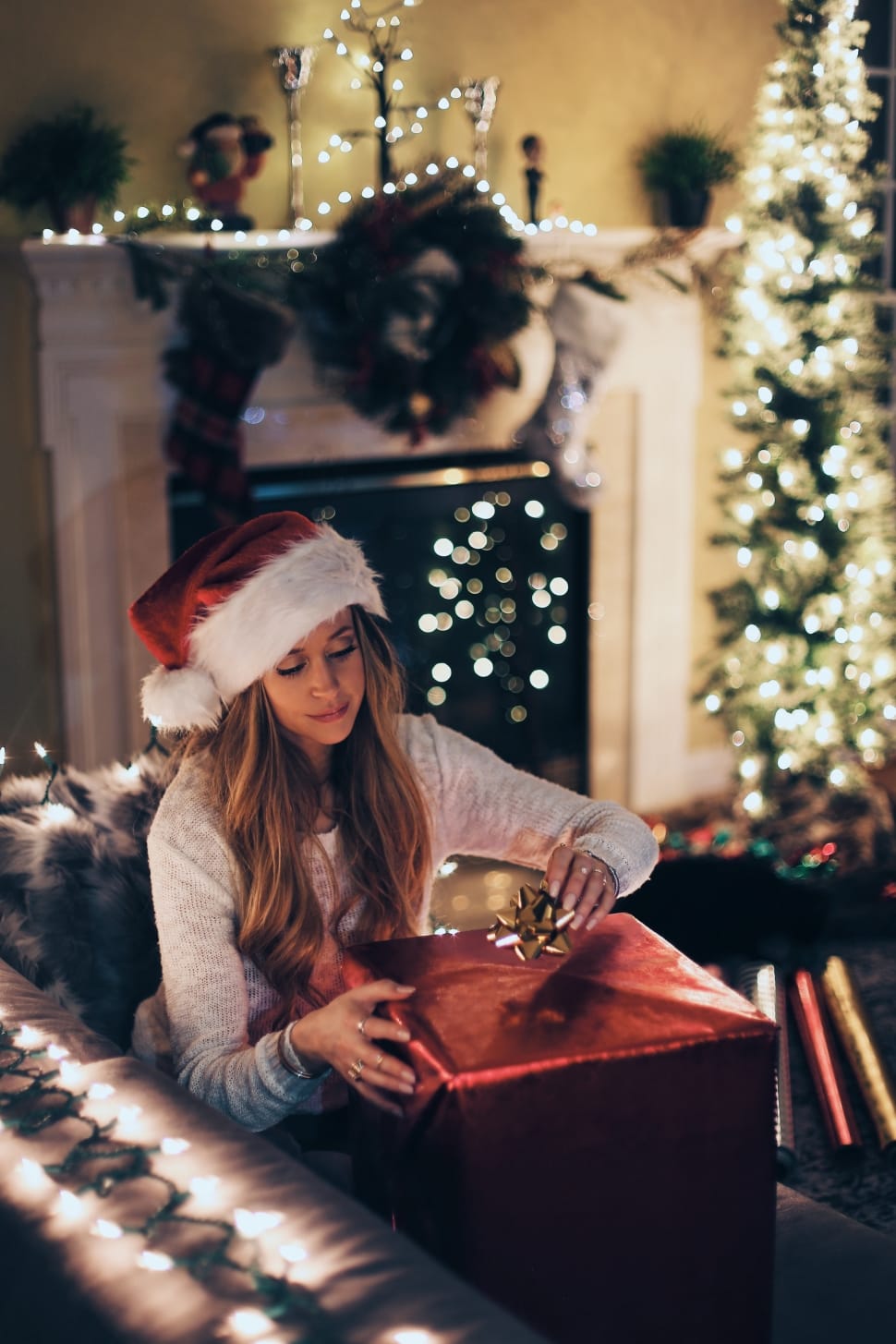 woman in white long sleeve shirt with white and red santa hat sitting on gray sofa preview