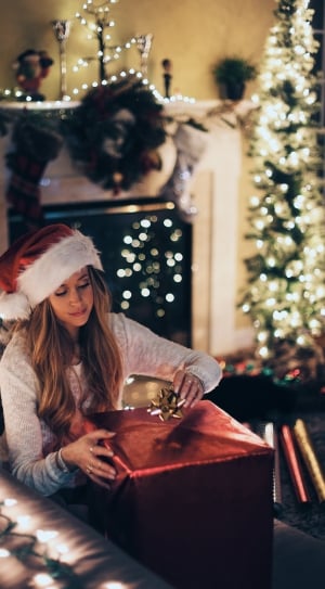 woman in white long sleeve shirt with white and red santa hat sitting on gray sofa thumbnail
